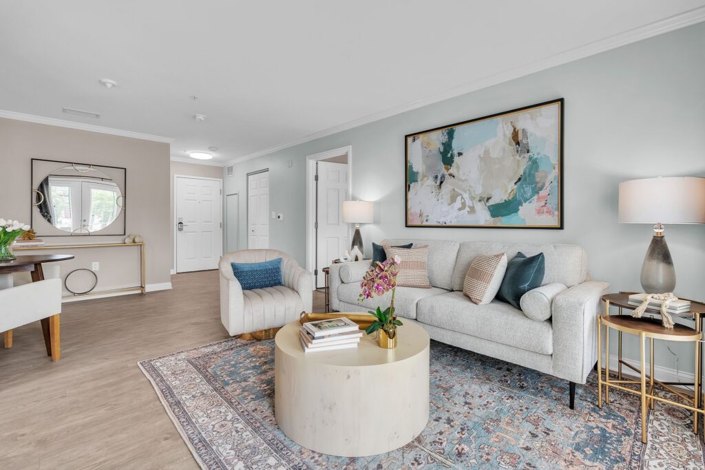 Modern living room with a light gray sofa, armchair, abstract wall art, and a patterned rug exudes luxury. A round coffee table with books and a plant sits centerstage. A desk with mirror is near the entry door in this inviting Hilliard, Ohio space.