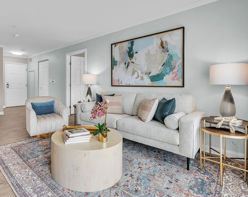 A modern living room in Hilliard, Ohio, with a light gray sofa, colorful pillows, side tables with lamps, and abstract wall art. Neutral tones and natural light make this the perfect cozy space for senior living.