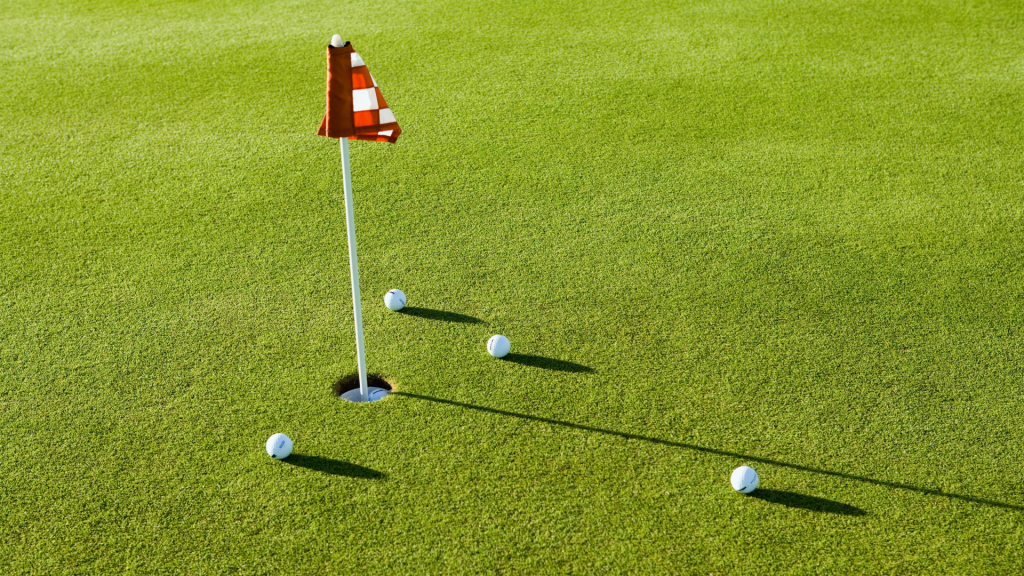 A red and white checkered flag in a golf hole on a green in Hilliard, Ohio, with four golf balls scattered around the hole casting shadows—perfect for senior living residents who enjoy an active lifestyle.
