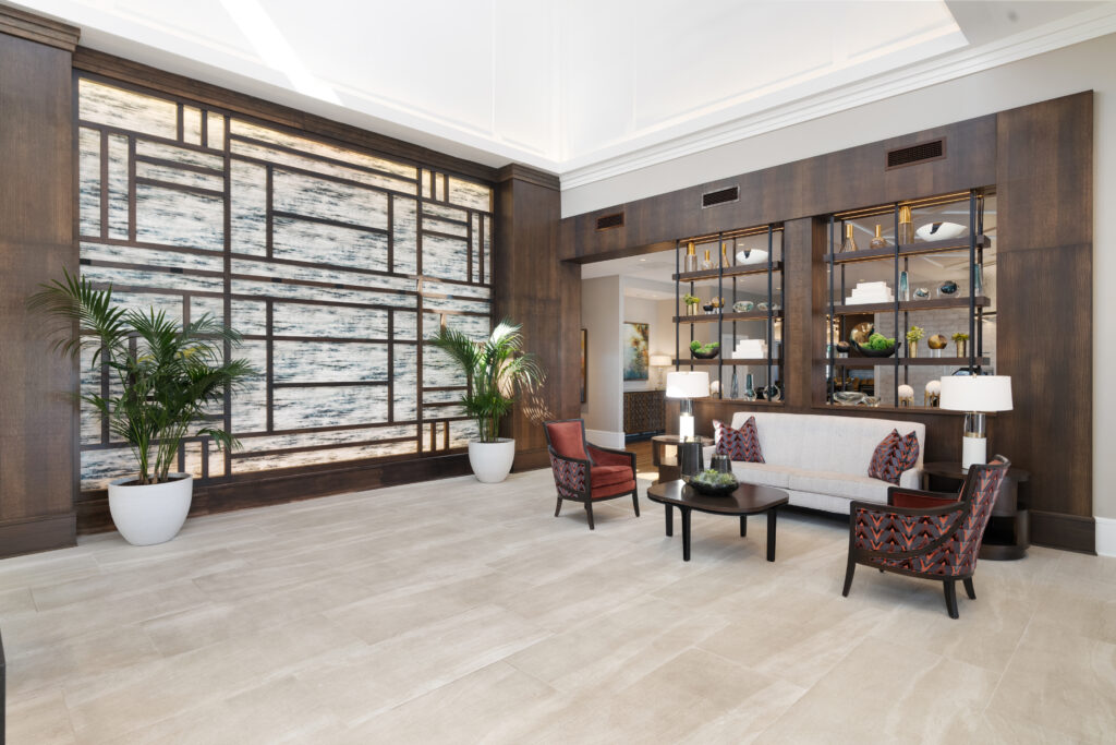 A modern, spacious lobby in Hilliard, Ohio features light tile floors, a white sofa, two patterned armchairs, potted plants, and built-in shelves—creating a luxury setting ideal for senior living.