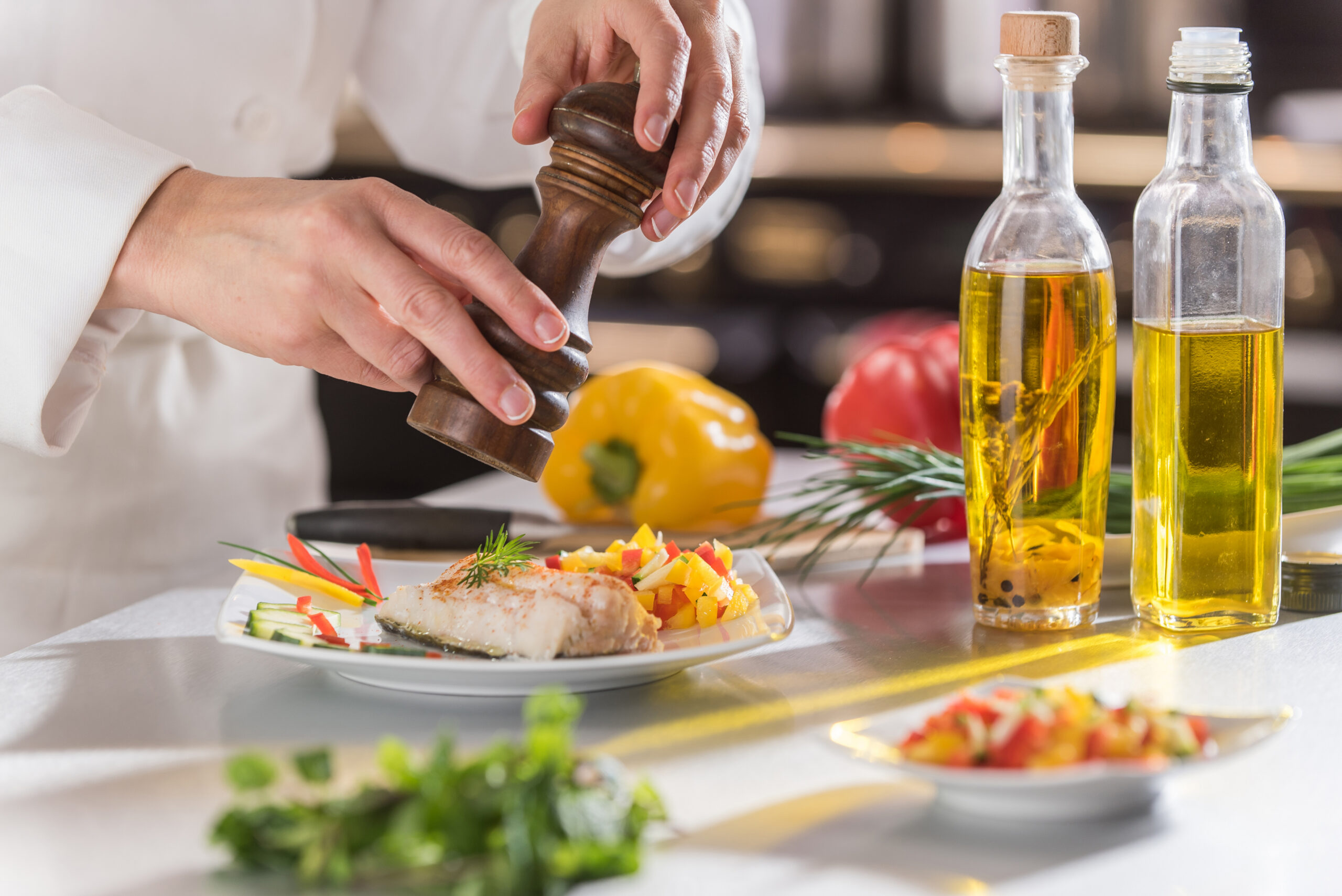 A chef’s hands grinding pepper onto a plated fish dish garnished with herbs and vegetables captures the vibrant, fresh cooking scene at this independent living community in Hilliard, Ohio. Bottles of oil, peppers, and herbs complete the inviting setting for seniors.